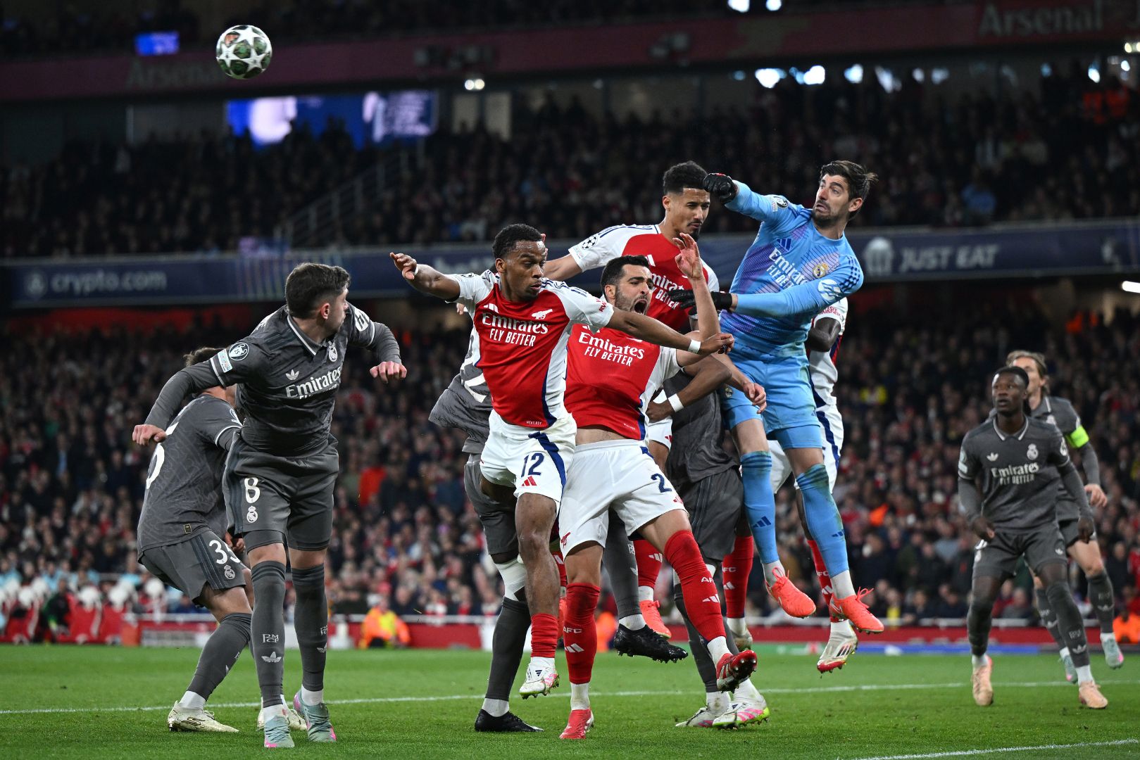 LONDON, ENGLAND - APRIL 08: Thibaut Courtois of Real Madrid punches the ball clear as Jurrien Timber, Mikel Merino and William Saliba of Arsenal challenge during the UEFA Champions League 2024/25 Quarter Final First Leg match between Arsenal FC and Real Madrid C.F. at Emirates Stadium on April 08, 2025 in London, England.